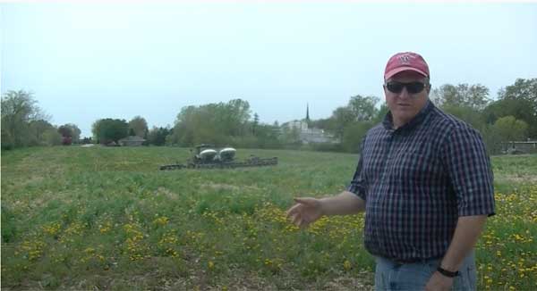 Man standing in farm field with tractor behind him
