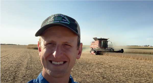 Man smiling with tractor on farm field behind him