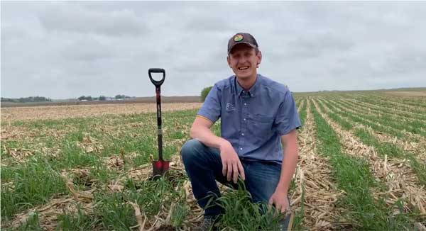 Man squatting in farm field with shovel beside him