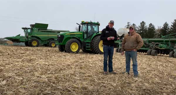 Two men standing in farm field with tractors