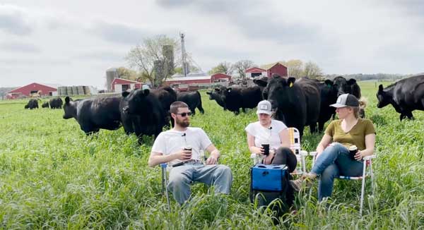 Man and two women sitting in lawn chairs with cows behind them