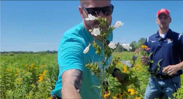 Man holding prairie flowers up to camera with another man in background